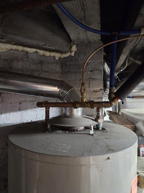 Responded to service call for non-functioning water heater approximately fifteen years old. Upon arrival, accessed utility area via back entrance as requested. Performed visual inspection of existing water heater unit and surrounding plumbing infrastructure. Documented condition of 15-year-old residential water heater, associated copper piping, brass fittings, pressure relief valve assembly, and connection points. Observed aged plumbing components with oxidation present on copper lines and galvanized steel piping. Photographed existing installation including top-mounted plumbing connections, PEX supply lines, and ventilation ductwork for reference. Provided estimate for complete water heater replacement as requested.
