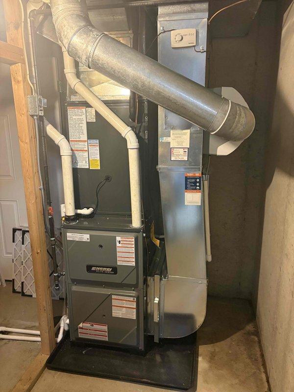 Completed full HVAC system installation including new residential furnace and outdoor air conditioning condenser unit. Furnace installed in basement utility area on protective base pad with proper PVC venting and condensate drainage system, metallic supply trunk ductwork connected and secured. Exterior AC condenser positioned on concrete pad with refrigerant lines run to house, electrical disconnect box mounted, and unit tested for proper operation.