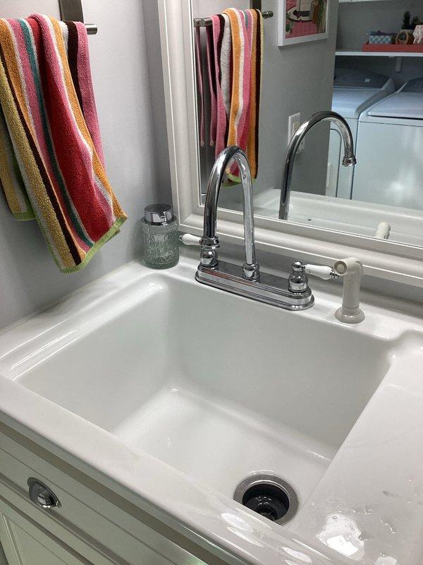 Responded to service call for dripping laundry room faucet and persistent odor from household drains. Inspected dual-handle chrome faucet at laundry sink and examined drain system beneath sink, including P-trap configuration and PVC plumbing connections. Addressed dripping faucet issue and assessed drain system for source of recurring foul odors affecting all sinks throughout the residence.