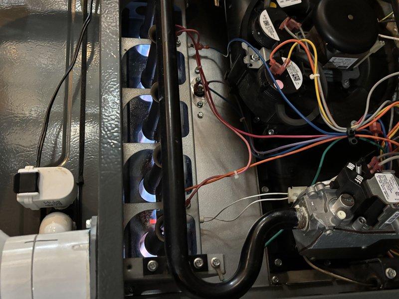 Completed exhaust and collector box repair on residential HVAC furnace unit. Accessed internal components through top panel, inspected gas burner assembly with multiple burner ports showing proper flame characteristics, and verified all electrical connections to motor, blower unit, and gas valve assembly. Examined and serviced exhaust venting system including PVC condensate drainage routing, flexible ductwork connections, and rigid duct sections to ensure proper airflow and safe operation of heating system.