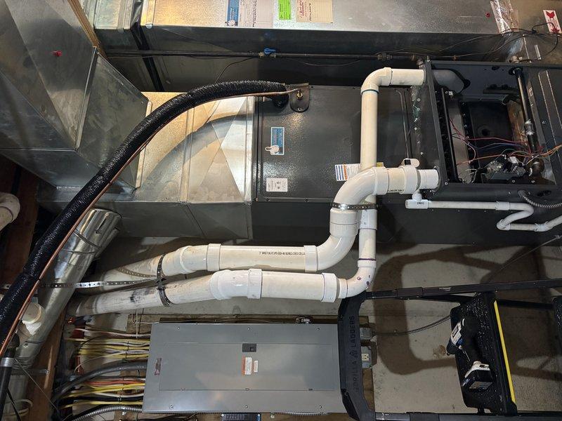 Completed exhaust and collector box repair on residential HVAC furnace unit. Accessed internal components through top panel, inspected gas burner assembly with multiple burner ports showing proper flame characteristics, and verified all electrical connections to motor, blower unit, and gas valve assembly. Examined and serviced exhaust venting system including PVC condensate drainage routing, flexible ductwork connections, and rigid duct sections to ensure proper airflow and safe operation of heating system.