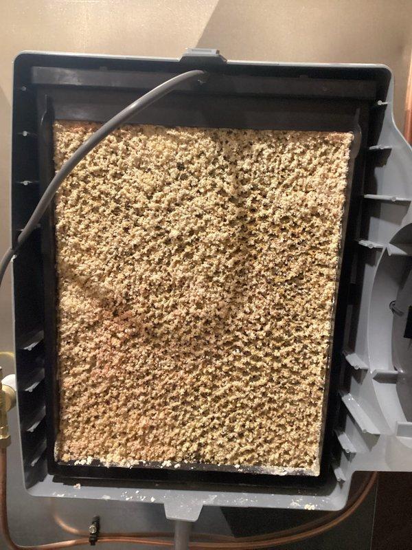 Responded to service call for malfunctioning humidifier system. Upon inspection, discovered evaporative humidifier pad was heavily clogged with dust, debris, and mineral deposits, completely obstructing airflow and preventing proper humidification. Removed and replaced saturated humidifier pad with new evaporative media filter, ensuring proper fit within mounting frame and reconnecting water distribution line. System tested and confirmed operational with adequate water flow and humidification output restored.