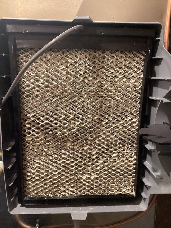 Responded to service call for malfunctioning humidifier system. Upon inspection, discovered evaporative humidifier pad was heavily clogged with dust, debris, and mineral deposits, completely obstructing airflow and preventing proper humidification. Removed and replaced saturated humidifier pad with new evaporative media filter, ensuring proper fit within mounting frame and reconnecting water distribution line. System tested and confirmed operational with adequate water flow and humidification output restored.