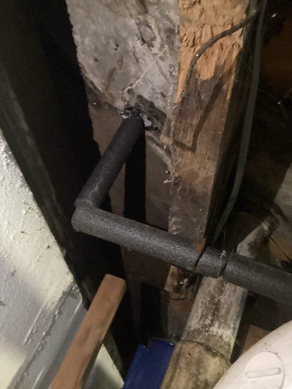 Responded to toilet service request where client required a taller toilet installation to meet accessibility needs. Assessed existing toilet condition in basement bathroom area, noting aged floor tile installation with visible wear and deterioration around base. Documented pre-existing conditions including damaged wooden structural post near plumbing lines showing moisture-related decay, and black foam-insulated utility pipes in adjacent utility space. Photographed work area showing standard floor-mounted toilet on dark tile flooring with accumulated debris and grout line discoloration. Coordinated service scheduling based on client availability constraints for future toilet replacement with ADA-compliant comfort height fixture.