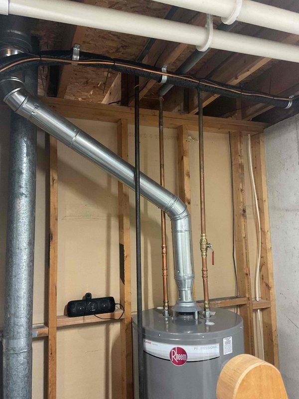 Evaluated existing Rheem water heater venting configuration in unfinished basement to determine feasibility of converting from vertical roof vent to horizontal side-wall vent termination. Inspected current Category I atmospheric vent system with metal exhaust pipe extending upward from unit, assessed clearances to combustible materials, and reviewed proximity to existing HVAC ductwork and PVC plumbing lines. Advised client on code requirements, structural considerations, and potential need for power venting conversion depending on appliance specifications and horizontal run length requirements.