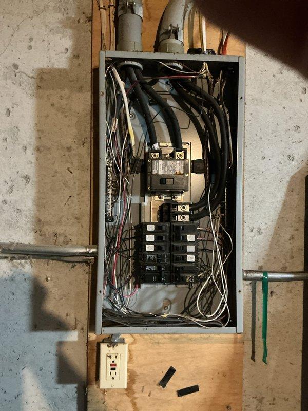 Conducted electrical estimate for running power to an outbuilding from existing main service panel. Assessed current panel capacity, circuit breaker availability, and wire routing requirements from basement-mounted electrical panel through structure to proposed outbuilding location. Documented existing panel configuration with multiple circuit breakers in dual columns, main disconnect assembly, and current wiring arrangements including conduit pathways along wooden framing. Photographed panel interior showing circuit organization, available breaker spaces, and wire management to determine feasibility and material requirements for new dedicated circuit installation to outbuilding.