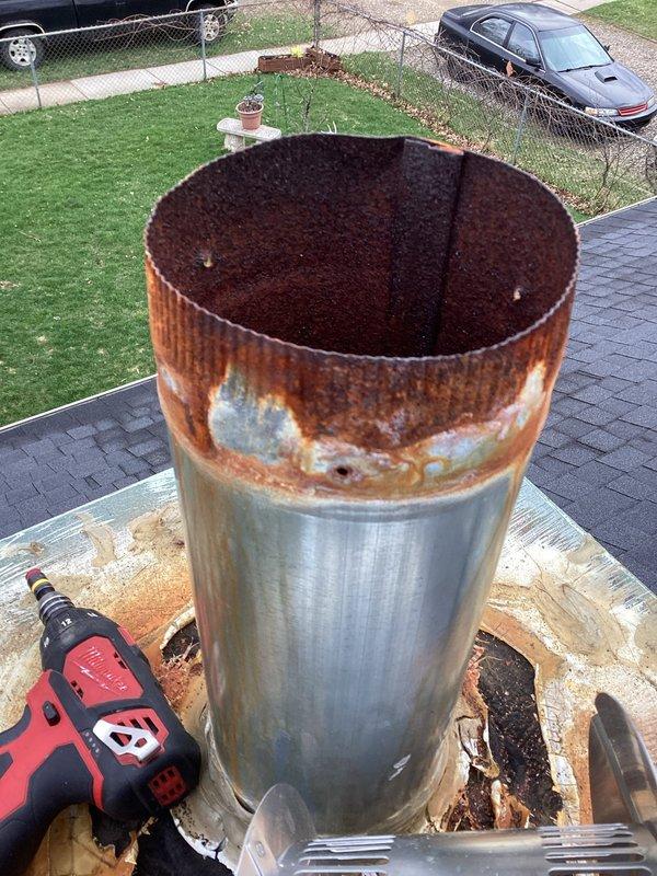 Responded to service call for missing chimney cap on residential property. Upon arrival, found chimney cap had blown off during recent weather event, leaving chimney liner exposed and vulnerable to water intrusion and debris. Inspection revealed extensive rust and corrosion on upper portion of existing chimney liner, with deteriorated material around rim indicating advanced age and weathering. Base platform showed significant rust staining and structural damage around pipe penetrations, with gaps and missing material creating potential water entry points.

Assessed condition of dual-pipe chimney system consisting of main flue pipe and secondary vent pipe, both requiring new protective caps. Documented existing damage through photographs showing corroded liner condition and compromised base integrity. Replaced missing chimney cap assembly with new stainless steel caps featuring dome-shaped tops and ventilation slots to ensure proper draft and weather protection for both pipes. Secured n