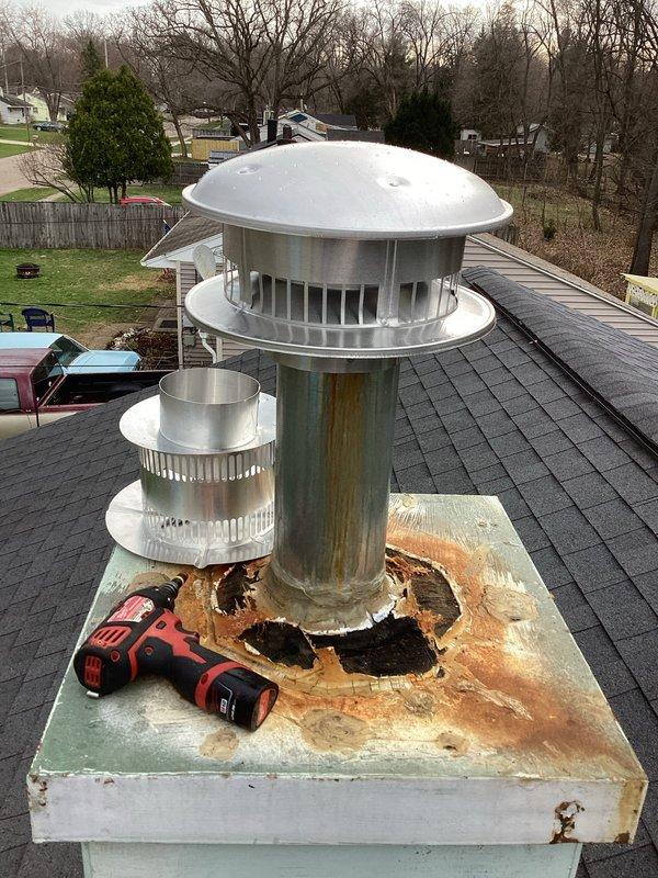 Responded to service call for missing chimney cap on residential property. Upon arrival, found chimney cap had blown off during recent weather event, leaving chimney liner exposed and vulnerable to water intrusion and debris. Inspection revealed extensive rust and corrosion on upper portion of existing chimney liner, with deteriorated material around rim indicating advanced age and weathering. Base platform showed significant rust staining and structural damage around pipe penetrations, with gaps and missing material creating potential water entry points.

Assessed condition of dual-pipe chimney system consisting of main flue pipe and secondary vent pipe, both requiring new protective caps. Documented existing damage through photographs showing corroded liner condition and compromised base integrity. Replaced missing chimney cap assembly with new stainless steel caps featuring dome-shaped tops and ventilation slots to ensure proper draft and weather protection for both pipes. Secured n