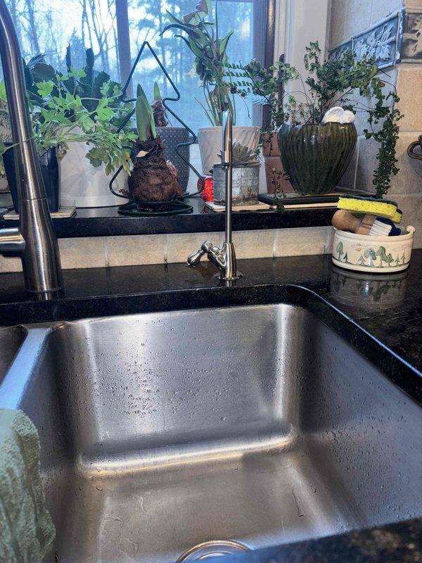 Installed customer-supplied reverse osmosis water filtration system under kitchen sink following countertop hole drilling for dedicated RO faucet. System was mounted to cabinet wall with white housing unit and filter canister, connected to cold water supply line with appropriate fittings, and integrated with existing plumbing infrastructure including drain saddle valve attachment to disposal unit tailpiece. Blue tubing was routed to newly installed countertop faucet, all connections were pressure tested for leaks, and system was flushed per manufacturer specifications to ensure proper operation.