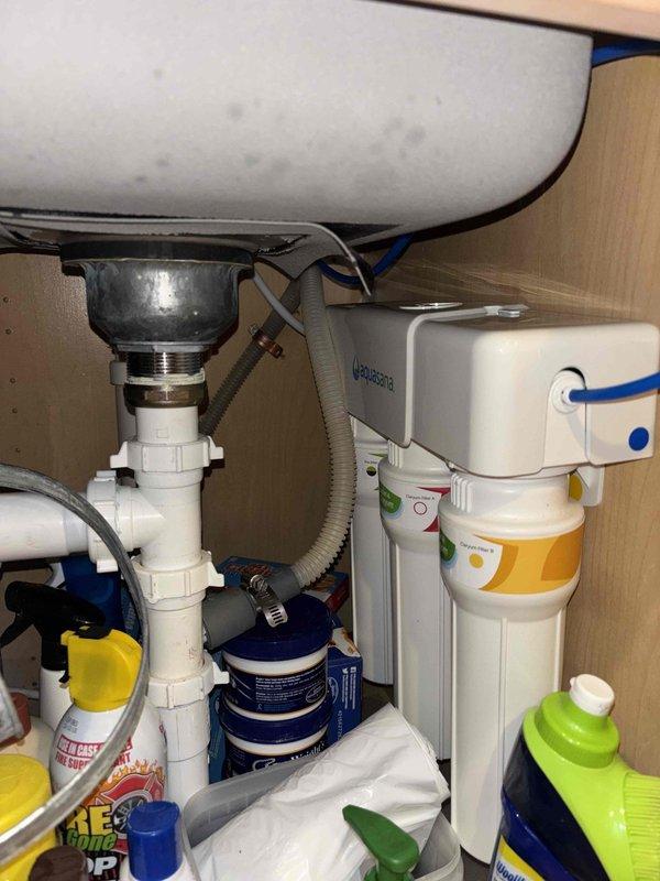 Installed customer-supplied reverse osmosis water filtration system under kitchen sink following countertop hole drilling for dedicated RO faucet. System was mounted to cabinet wall with white housing unit and filter canister, connected to cold water supply line with appropriate fittings, and integrated with existing plumbing infrastructure including drain saddle valve attachment to disposal unit tailpiece. Blue tubing was routed to newly installed countertop faucet, all connections were pressure tested for leaks, and system was flushed per manufacturer specifications to ensure proper operation.