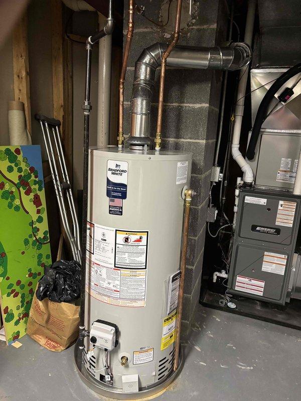 Successfully completed full installation of new furnace and water heater system in residential basement utility area. Installed dark gray forced-air furnace unit with proper venting configuration, including white PVC exhaust piping routed to ceiling-mounted black ductwork. Mounted furnace on protective drip pan per code requirements. Connected all electrical conduit and wiring to furnace unit.

Installed Bradford White water heater adjacent to furnace system with copper supply line connections and metallic elbow duct at top of unit. Secured all gas lines and water lines to wall structure with proper mounting hardware. Verified all manufacturer specifications and safety labels are visible and intact on both units.

Completed all ductwork connections between furnace and air distribution system. Ensured proper clearances maintained around both units for service access and code compliance. System tested and confirmed operational upon completion.