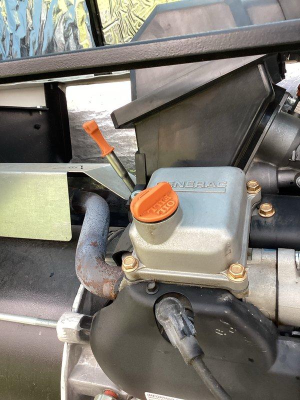 Completed first scheduled maintenance visit on 5-year-old Generac generator unit under recurring service plan. Addressed battery alert indication displayed on control panel. Performed comprehensive inspection of generator components including engine assembly, fuel system, and electrical connections. Verified oil level at dipstick reservoir and inspected condition of all fluid lines and hoses. Checked security of all mounting hardware and connection clamps throughout the unit. Examined fuel shut-off valve operation and associated piping. Inspected engine compartment insulation and ventilation components for proper condition. Documented equipment status with photographic records showing current operational configuration and component conditions. All systems verified functional following inspection protocol.