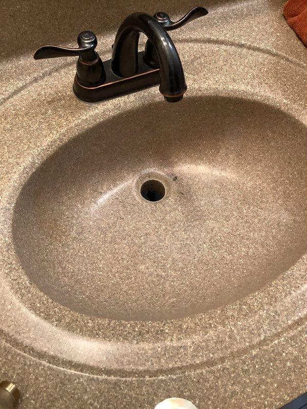 Returned to property to install customer-supplied pop-up drain assembly in master bathroom sink. Removed existing chrome drain stopper and cleaned mineral deposits and hard water buildup from basin and drain area. Installed new pop-up assembly, ensuring proper alignment and seal with integrated countertop sink, then tested operation to verify smooth functionality and proper drainage.