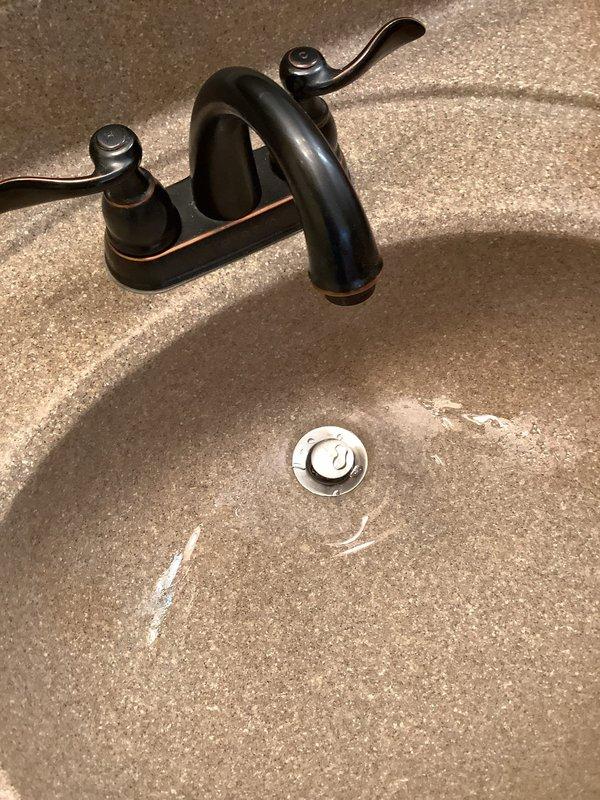 Returned to property to install customer-supplied pop-up drain assembly in master bathroom sink. Removed existing chrome drain stopper and cleaned mineral deposits and hard water buildup from basin and drain area. Installed new pop-up assembly, ensuring proper alignment and seal with integrated countertop sink, then tested operation to verify smooth functionality and proper drainage.