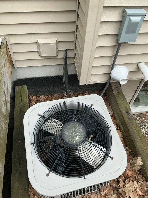 Provided estimate for air conditioning system replacement at residential property. Inspected existing outdoor condenser unit with white cabinet and black fan grille, noting unit positioned against house exterior on concrete pad within timber-framed recessed area. Customer expressed interest in current promotional offerings for new AC system installation.
