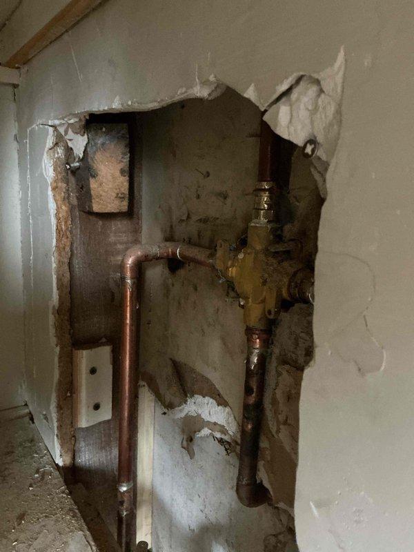 Responded to plumbing leak caused by improper DIY shower component installation. Opened drywall to access plumbing system and identified faulty connections in copper supply lines and brass valve assembly. Repaired leaking fittings, verified proper installation of shower components, and confirmed all connections were secure and leak-free before closing access point.