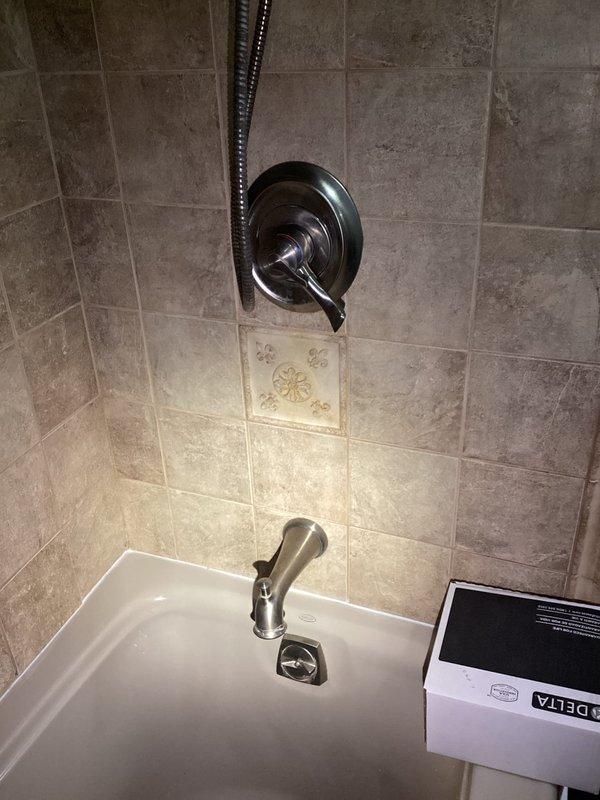 Replaced faulty shower valve assembly in bathroom. Accessed plumbing by opening wall cavity from adjacent room, removed old valve cartridge and trim, installed new chrome single-handle shower control with coordinating tub spout and flexible shower hose assembly, then restored wall opening. All fixtures tested and operating properly with no leaks detected.