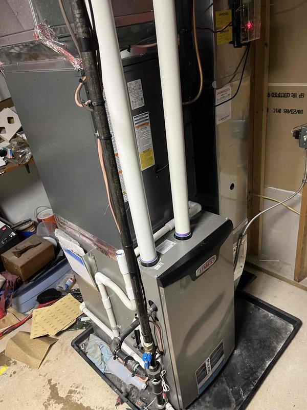 Completed full HVAC system installation including indoor furnace unit and outdoor condensing unit. Installed furnace in basement mechanical room with proper venting using white PVC intake and exhaust pipes, secured copper refrigerant lines with black insulation, and connected condensate drainage with shutoff valves on drain pan. Positioned outdoor condenser unit on concrete pad against foundation, ran electrical conduit to disconnect box, and verified all refrigerant line connections between indoor and outdoor equipment for proper system operation.