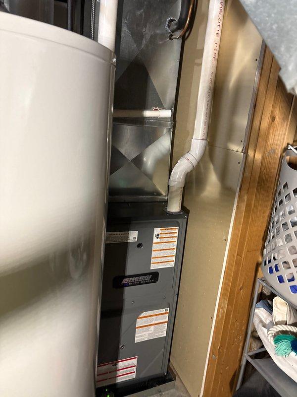 Completed full furnace replacement in residential utility closet. Installed new dark gray furnace unit with proper vertical positioning and secured all manufacturer safety labels. Connected silver metal supply ductwork to unit discharge with appropriate angles and sealed all joints. Installed white PVC condensate drain and vent piping along right side of unit with secure mounting. Verified proper clearances from adjacent water heater and surrounding walls per code requirements. Tested all electrical connections, gas line integrity, and airflow distribution. System commissioned and operational, meeting manufacturer specifications.