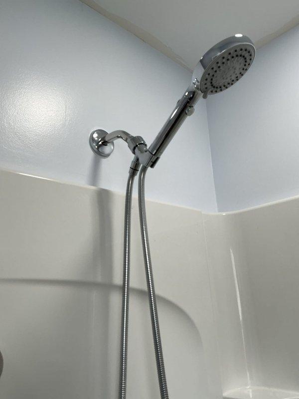 Completed installation of handheld shower head assembly with flexible metal hose and chrome wall mount bracket in fiberglass shower enclosure. Installed under-sink plumbing configuration including P-trap assembly, supply line connections, and faucet tailpiece with braided metal supply lines, completing work from previous project phase.