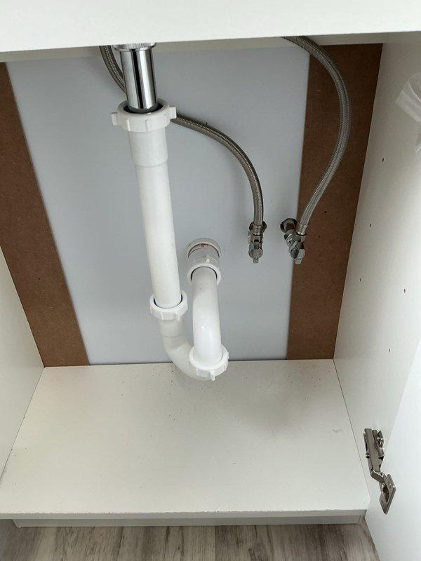 Completed installation of handheld shower head assembly with flexible metal hose and chrome wall mount bracket in fiberglass shower enclosure. Installed under-sink plumbing configuration including P-trap assembly, supply line connections, and faucet tailpiece with braided metal supply lines, completing work from previous project phase.