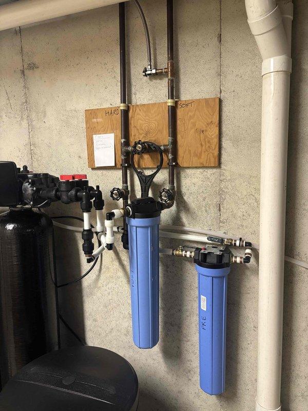 Responded to water pressure complaint following recent repair work. Inspected whole-house water treatment system including dual blue filter housings, water softener tank, and pressure tank. Identified potential restriction in filtration system causing reduced flow. Evaluated filter cartridges for blockage, checked valve positions, and verified proper system operation. Documented existing equipment condition and configuration with photos for service records.