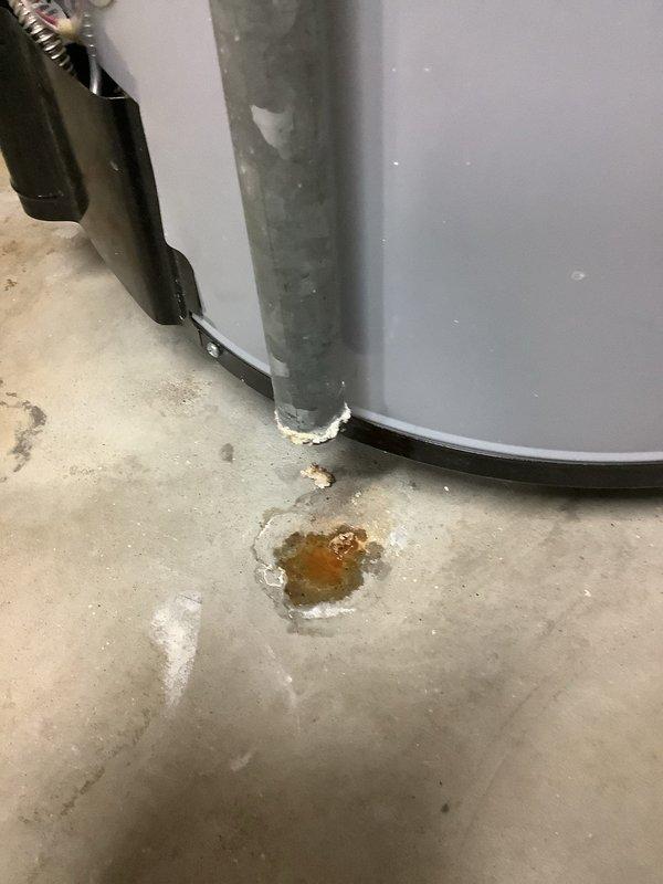 Completed annual cooling maintenance on 23-year-old American Standard air conditioning system. During routine inspection, discovered water heater in same utility area showing active leak at base with amber-colored water pooling on concrete floor and white mineral deposits indicating previous leakage. Photographed water heater condition and temperature/pressure relief valve assembly for documentation. Advised customer of water heater failure requiring immediate attention to prevent further water damage.