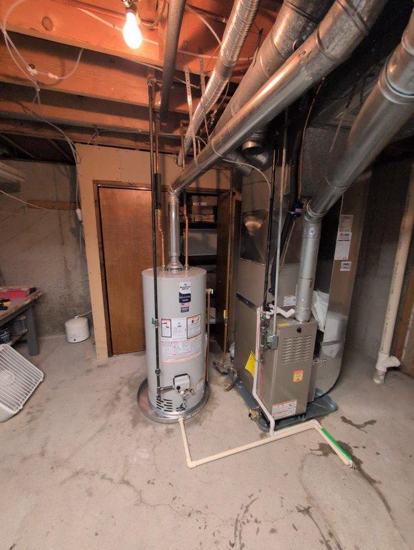 Successfully completed water heater installation in basement mechanical room. Removed existing unit and installed new white cylindrical water heater with proper venting and connections. Connected metal vent pipe extending to ceiling ductwork system, ensuring proper exhaust ventilation. Verified all plumbing connections, gas lines, and safety features are functioning correctly. Unit positioned on concrete floor alongside existing HVAC equipment with adequate clearance for maintenance access. All manufacturer specifications followed during installation, including proper TPR valve installation and drain pan placement. System tested and operational upon completion.