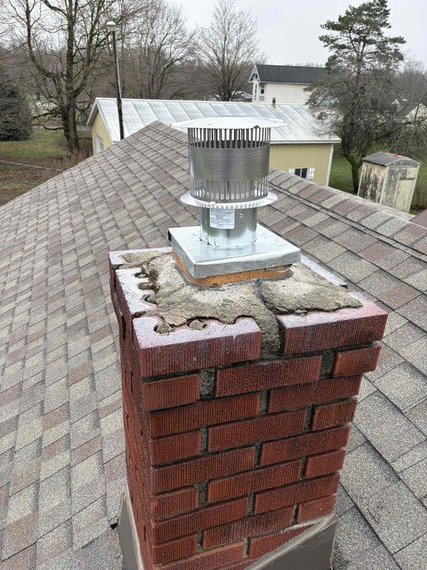 Performed no-charge inspection of chimney liner and cap system. Confirmed metal chimney cap is present and properly installed on brick chimney, though chimney crown shows significant deterioration with visible cracks and missing sections. Inspected basement mechanical room and verified flexible metallic liner connection to vertical exhaust system is secure and properly routed through PVC and metal ductwork assembly.