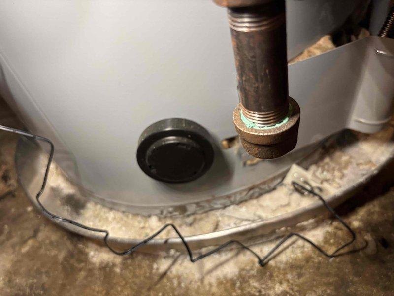 Responded to service call for 7-year-old water heater producing lukewarm water with reduced heating performance. Performed diagnostic inspection and tune-up service on unit. Inspected tank condition, heating elements, thermostat settings, and plumbing connections. Noted visible corrosion on threaded pipe connections and brass fittings, typical of unit age. Verified no active leaks present. Documented equipment condition with photos showing corroded pipe threading, tank mounting, and floor area beneath unit. Adjusted system settings as needed to restore proper water temperature output.