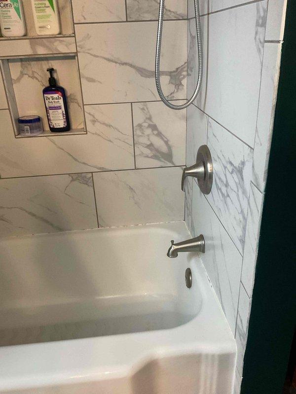 Responded to intermittent water pressure loss occurring during high-volume water usage in shower and dishwasher operation, issue originating after water heater replacement. Inspected plumbing system and fixtures to diagnose pressure fluctuation requiring temporary shutoff periods for recovery. Addressed loose shower faucet handle unable to maintain proper downward orientation due to mounting hardware issue. Documented bathroom shower installation featuring brushed nickel fixtures, handheld showerhead assembly, and tiled surround for service records.