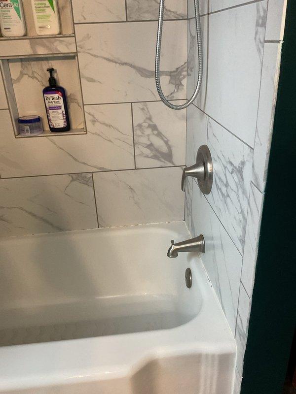 Responded to intermittent water pressure loss occurring during high-volume water usage in shower and dishwasher operation, issue originating after water heater replacement. Inspected plumbing system and fixtures to diagnose pressure fluctuation requiring temporary shutoff periods for recovery. Addressed loose shower faucet handle unable to maintain proper downward orientation due to mounting hardware issue. Documented bathroom shower installation featuring brushed nickel fixtures, handheld showerhead assembly, and tiled surround for service records.