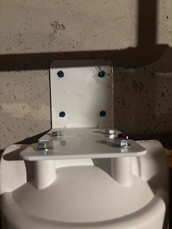 Returned to property to correct the mounting installation of a wall-mounted water filter housing. The filter's mounting bracket had been improperly secured to the overhead support structure, requiring adjustment of the chrome mounting bolts and repositioning of the white metal mounting plate against the ceiling beam. Verified proper alignment of the filter housing with the copper supply piping and ensured all mounting hardware was tightened to manufacturer specifications for secure, long-term installation.