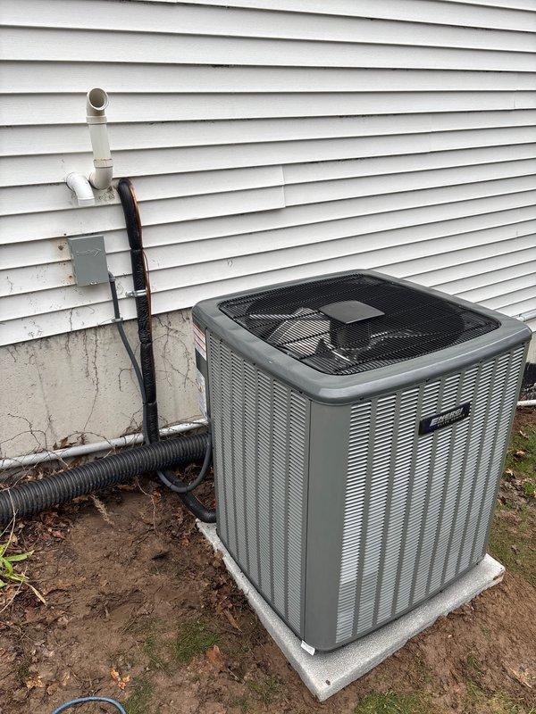 Completed full installation of residential air conditioning system including outdoor condenser unit mounted on concrete pad against exterior wall. Installed and secured all refrigerant lines, electrical connections via junction box, drainage components with PVC piping, and flexible conduit runs. Verified all connections, applied proper sealing and protection to penetrations through building envelope, and confirmed system operational status with appropriate labeling affixed to unit per manufacturer specifications.