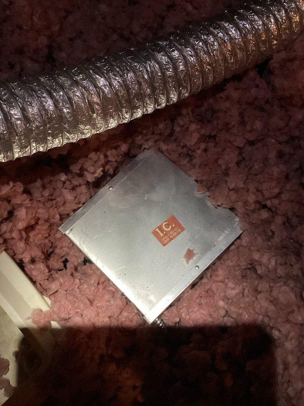 Responded to water leak complaint regarding attic fan over garage. Upon inspection, found condensation dripping from attic ventilation fan unit. System was shut off at time of arrival to prevent further water intrusion. Accessed attic space and inspected fan assembly, flexible metallic ductwork, and surrounding insulation for moisture damage. Documented conditions with photos showing the circular fan unit with central motor housing mounted in wooden frame structure and silver spiral-ribbed HVAC duct running through insulated attic space. Pink fiberglass insulation present throughout area with metal access panel visible. Confirmed condensation issue related to attic fan operation and verified system remains in off position pending further evaluation or repair recommendations.