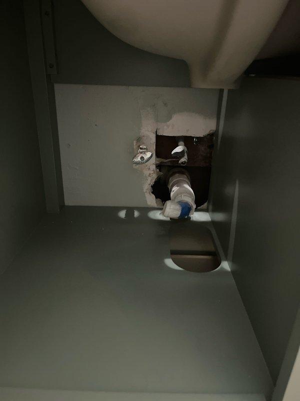 Conducted comprehensive plumbing assessment for new vanity installation, refrigerator ice maker connection, and basement bathroom plumbing issue. Inspected existing under-sink cabinet infrastructure, documenting current drain assembly configuration with white PVC P-trap system and flexible braided supply lines. Evaluated cabinet access points and existing rough-in openings to determine requirements for new vanity plumbing connections, ice maker water supply line routing, and basement bathroom repairs.