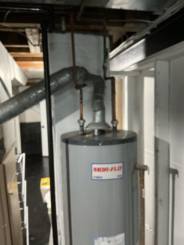 Completed water heater estimate for existing MOR-FLO unit located in basement utility area. Assessed current installation including supply and discharge piping connections, shut-off valves, and venting configuration. Documented equipment specifications and provided replacement options for client consideration.