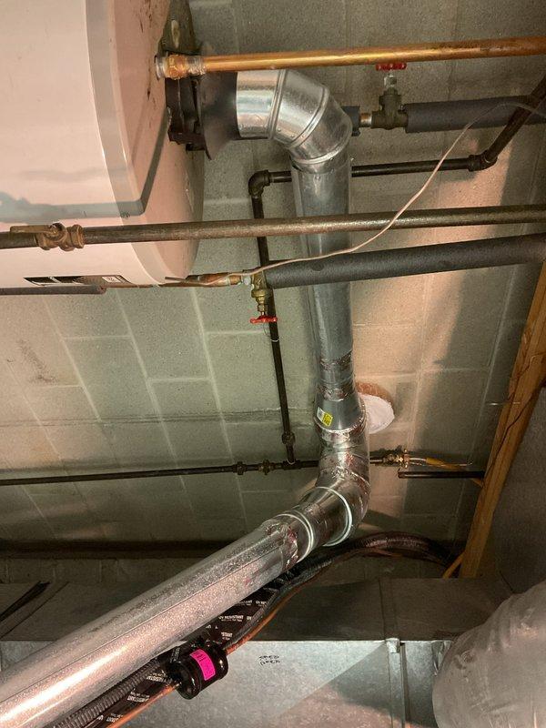 Responded to complaint of rusty water from 10-year-old water heater. Upon inspection, found significant corrosion on water heater system and associated copper plumbing. Documented existing conditions of basement utility area including water heater connections, copper supply lines, and HVAC ductwork routing. Photographed metallic ductwork elbows, copper piping with visible oxidation, red valve control mechanisms, and insulated refrigerant lines for service records. Advised customer that rust-colored water typically indicates deterioration of anode rod or internal tank corrosion in aging water heater units, and recommended replacement evaluation given unit age and symptom severity.