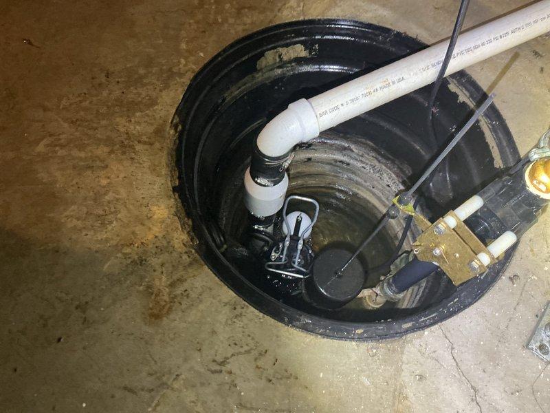 Responded to service call for sump pump disconnected from check valve assembly. Upon arrival, found submersible sump pump separated from discharge piping within basin. Reconnected pump to white PVC discharge pipe and check valve, ensuring proper alignment and secure fitting at elbow joint connection. Verified all plumbing connections were tight and leak-free. Tested pump operation to confirm proper discharge flow through piping system and check valve functionality. System restored to normal working condition.