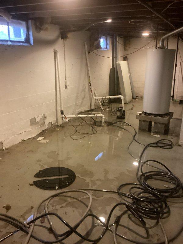 Responded to sump pump failure causing significant water accumulation in basement. Upon arrival, found extensive standing water throughout the concrete floor with multiple areas of pooling. Inspected existing sump pump system and found the pump operational but inadequate for current water intrusion levels. Assessed basin for proper depth and drainage, noting sediment and rust accumulation in standing water. Deployed emergency water extraction equipment using portable pumps and hoses to remove immediate flooding from basement floor. Cleared debris from sump basin and verified discharge line functionality. Recommended ongoing monitoring of water table levels and potential upgrade to higher capacity pump system to prevent future basement flooding events.