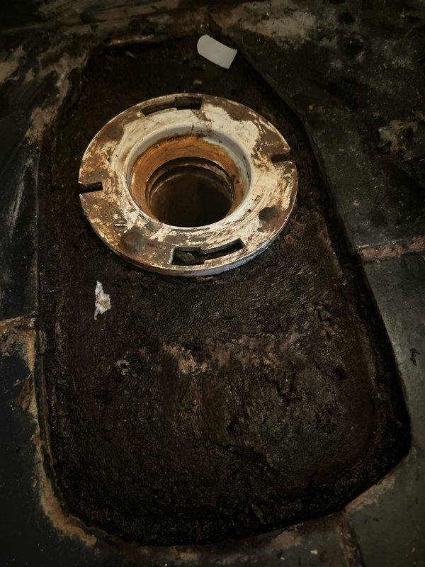 # Toilet Replacement and Repair

Removed and replaced deteriorated toilet due to extensive water damage to the subfloor and mounting area. The existing fixture had caused significant moisture infiltration, resulting in severe wood rot and structural degradation of the flooring beneath. Disconnected water supply line and removed corroded closet flange assembly showing heavy rust and mineral buildup.

Assessed subfloor damage and addressed compromised wooden planks exhibiting blackened discoloration and decay from prolonged moisture exposure. Removed affected flooring sections and prepared surface for new installation. Cleaned and scraped mounting area to remove accumulated debris, corrosion, and deteriorated material around drain opening.

Installed new wax ring seal and secured toilet to repaired mounting surface. Reconnected water supply line and tested for proper function and seal integrity. Verified no leaks at connection points and confirmed proper drainage operation. Restored area