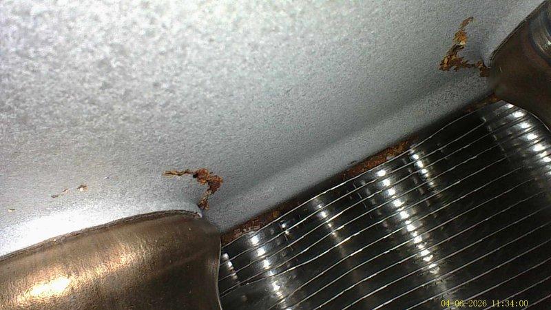 Completed annual cooling maintenance on a 15-year-old air conditioning system. Performed standard tune-up procedures including system inspection, refrigerant line examination, and evaporator coil assessment. Documentation revealed significant rust and corrosion present at the evaporator coil mounting points, with visible deterioration along the top edge where the coil assembly meets the mounting surface. Observed rust-colored staining and water damage on adjacent ceiling surfaces, indicating moisture infiltration or condensation issues. Copper refrigerant lines showed age-appropriate patina and weathering consistent with the system's service life. The finned coil assembly displayed metallic corrosion with rust transfer to surrounding white surfaces, suggesting ongoing moisture exposure that may compromise system efficiency and longevity if left unaddressed.