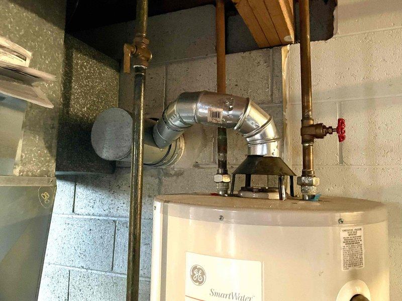 Responded to service call for slow leak at bottom of water heater. Upon inspection, identified active leak originating from base of tank on 20+ year old GE SmartWater unit installed in basement utility area. Leak consistent with internal tank corrosion and rust deterioration typical of units exceeding expected service life. Documented existing installation showing copper supply piping with shutoff valves, metallic vent connector, and standard residential water heater configuration. Photographed unit condition, plumbing connections, and evidence of tank failure. Provided estimate for complete water heater replacement due to compromised tank integrity beyond economical repair.