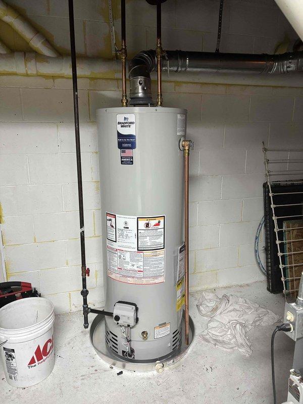 Successfully completed installation of a 40-gallon Bradford White natural draft natural gas water heater in residential basement utility room. Removed existing unit and installed new water heater with proper copper supply line connections, gas line hookup using flexible yellow CSST connector, temperature and pressure relief valve with discharge piping, and horizontal vent pipe properly secured to ceiling joists. All connections tested and verified operational with no leaks detected.