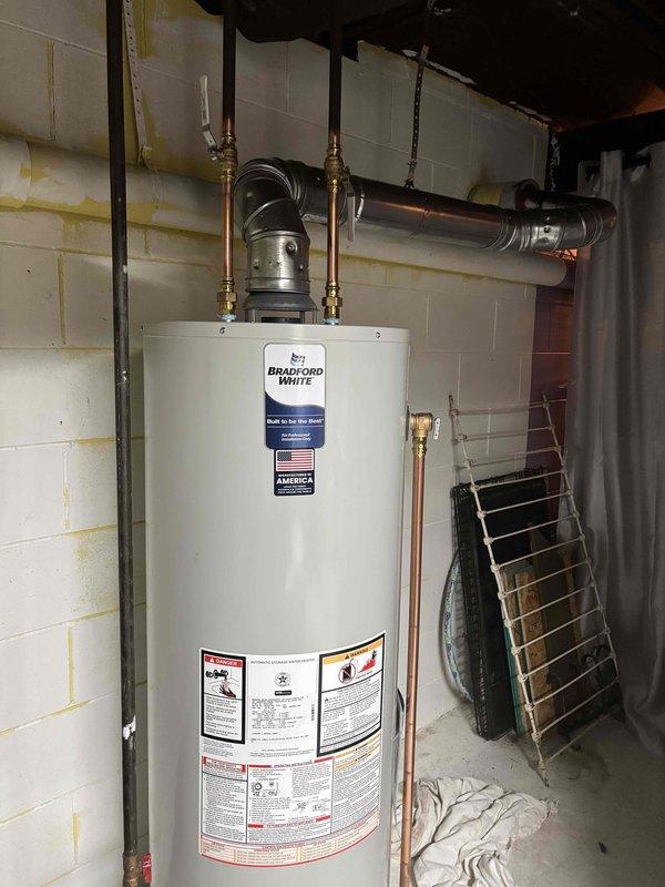 Successfully completed installation of a 40-gallon Bradford White natural draft natural gas water heater in residential basement utility room. Removed existing unit and installed new water heater with proper copper supply line connections, gas line hookup using flexible yellow CSST connector, temperature and pressure relief valve with discharge piping, and horizontal vent pipe properly secured to ceiling joists. All connections tested and verified operational with no leaks detected.