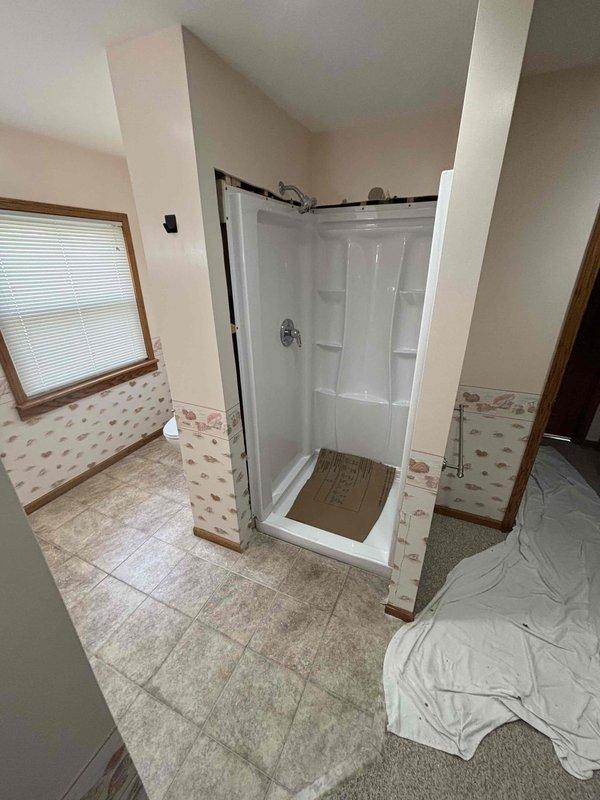 Completed full bathroom plumbing installation for shower system in residential upstairs bathroom with vaulted ceiling. Installed new white fiberglass shower stall with built-in corner shelving, chrome shower head, and control valve assembly with proper mounting and secure connections. Ran and secured all necessary supply lines including PVC and metal piping through wall framing, ensuring proper code compliance and structural integrity. Installed shower base/pan with appropriate waterproofing and drainage connections. All fixtures tested for proper water flow, temperature control, and leak-free operation upon completion.