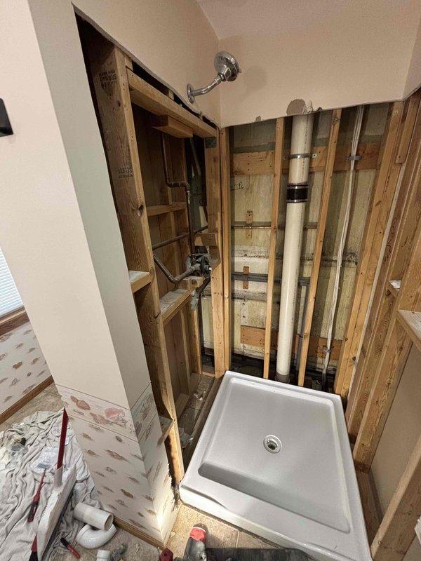 Completed full bathroom plumbing installation for shower system in residential upstairs bathroom with vaulted ceiling. Installed new white fiberglass shower stall with built-in corner shelving, chrome shower head, and control valve assembly with proper mounting and secure connections. Ran and secured all necessary supply lines including PVC and metal piping through wall framing, ensuring proper code compliance and structural integrity. Installed shower base/pan with appropriate waterproofing and drainage connections. All fixtures tested for proper water flow, temperature control, and leak-free operation upon completion.