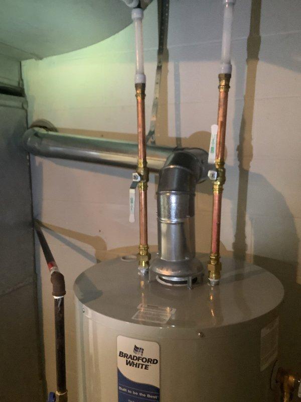 Completed comprehensive plumbing project involving water line repiping and installation of a 40-gallon Bradford White natural draft natural gas water heater with chimney liner. The installation features proper copper piping connections with brass fittings at the tank top, transitioning to PVC for venting, along with a circulation pump mounted horizontally across the supply lines and appropriate safety components including pressure relief valve. New gray PVC water supply lines were run vertically along the basement wall with shut-off valves installed at accessible mid-points for future maintenance access. The chimney liner was properly installed to ensure safe venting of combustion gases from the natural draft water heater. All plumbing connections were completed to code with proper support and securing of pipes, and the system was tested for leaks and proper operation. The two-day project included complete removal of old water lines and installation of new copper repiping throughout th