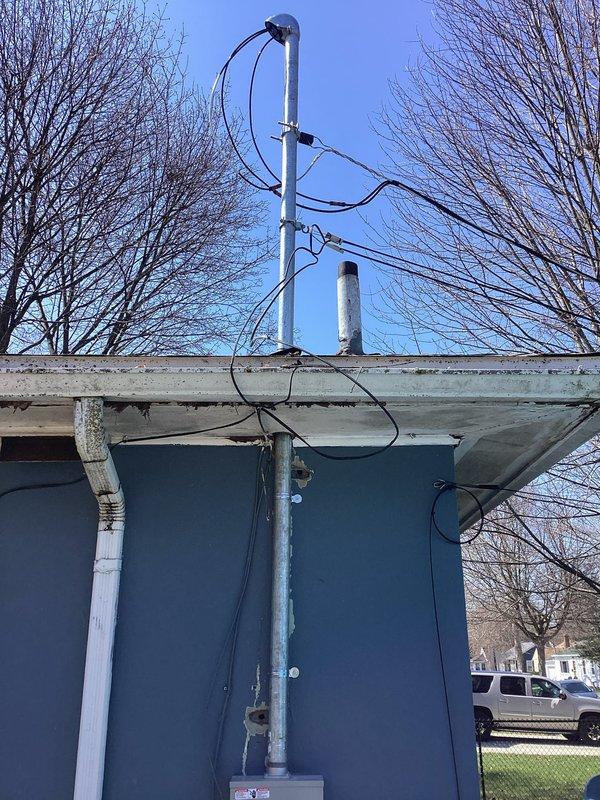 Completed electric service upgrade including coordination with utility company for temporary power disconnect and reconnect. Obtained electrical permit PE26-0355 and scheduled required inspection. Upgraded exterior meter assembly with new gray metal enclosure boxes, circular glass-covered electric meter, and associated junction boxes mounted on building exterior wall. Installed galvanized metal conduit painted white running vertically along wall for proper wire routing. Connected black electrical service wires from meter assembly through conduit system. Passed final electrical inspection and restored power to residence.