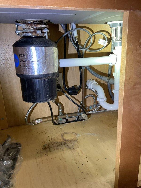 Responded to kitchen sink drainage issue. Upon arrival, found dual-basin stainless steel sink with garbage disposal unit experiencing complete blockage preventing water flow. Inspected under-sink plumbing configuration including black garbage disposal unit, white PVC drain lines, and trap assembly. Cleared obstruction from disposal unit and drain line using appropriate drain cleaning methods. Verified proper drainage flow in both sink basins. Tested garbage disposal operation and confirmed restored functionality. Checked all connections for leaks and verified system integrity before completion.